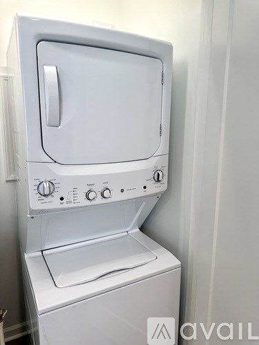 A white washing machine with a grey door and a grey handle is in a room with white walls.