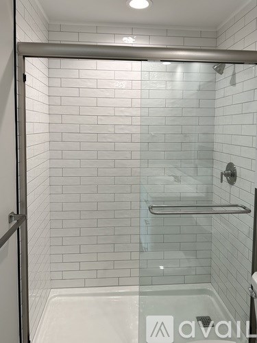 A white tiled shower with a glass door and a silver handle.