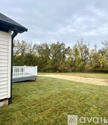 A white house with a porch and a yard with trees in the background.