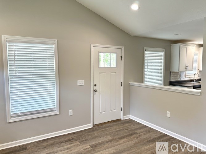 A room with a white door, a window with blinds, and a counter with a sink.