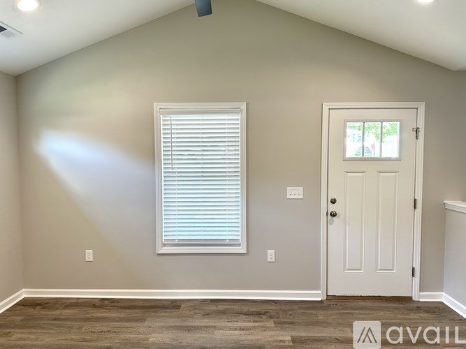 A room with a white door, window with blinds, and a wooden floor.