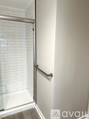 A white tiled shower with a glass door and a silver grab bar.