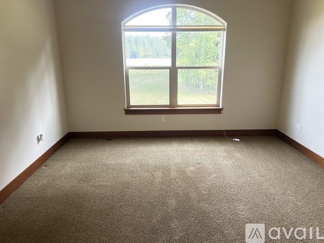 A carpeted room with a large window overlooking a grassy field.