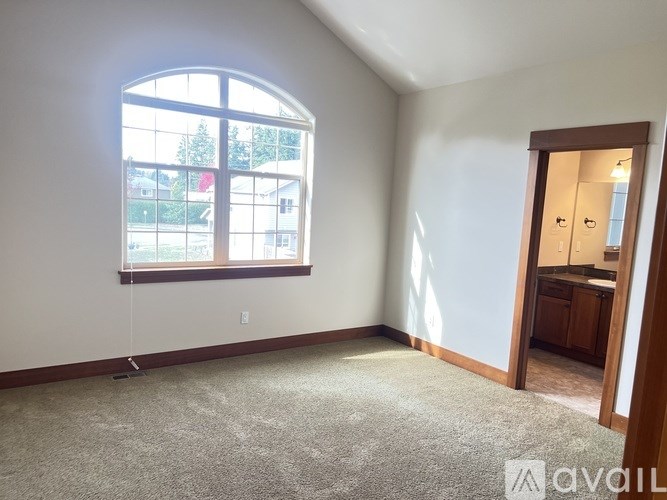 A carpeted room with a large window and a door leading to a kitchen.