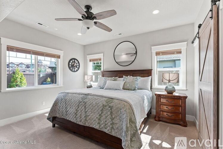 A bedroom with a large bed, a ceiling fan, and a window with a view of a tree.