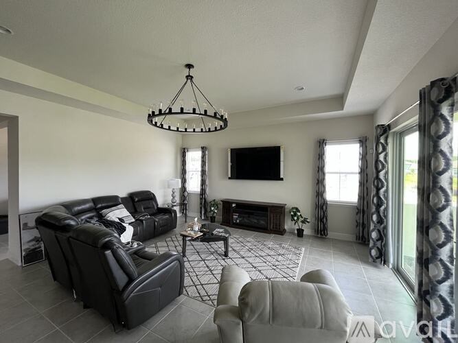 A living room with a black leather couch and a chandelier.
