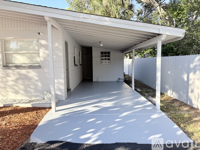 A white covered porch area with a white fence and trees in the background.