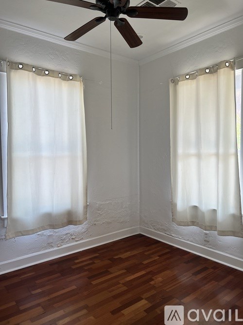 A room with a ceiling fan and two windows with curtains.