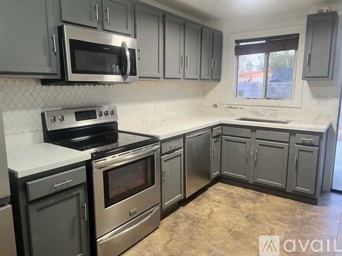 A kitchen with stainless steel appliances and grey cabinets.