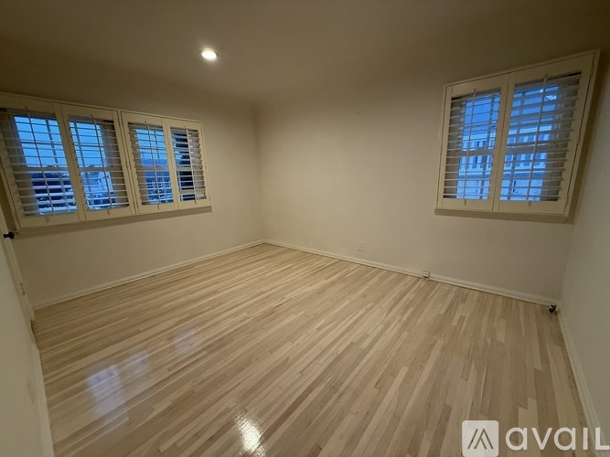 A room with wooden flooring and two windows with blinds.