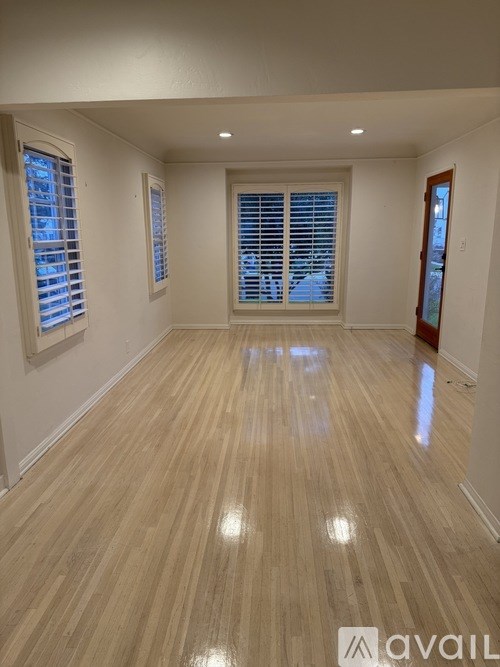 A room with wooden flooring and two windows with blinds.