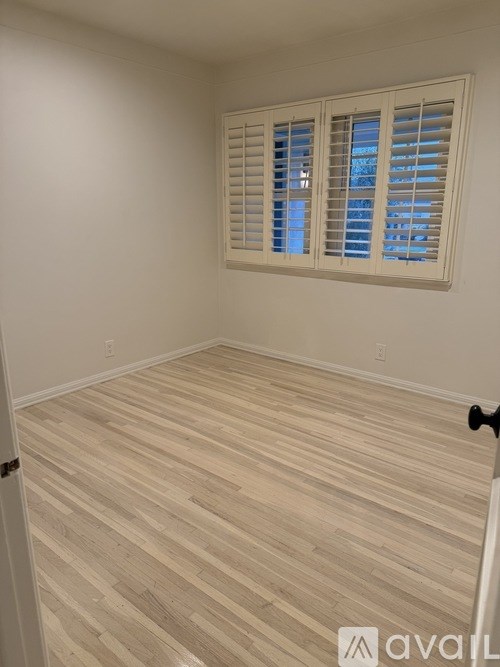 A room with wooden flooring and a window with blinds.