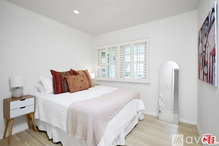 A bedroom with a white bed and a wooden nightstand.