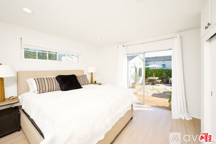 A bedroom with a large bed and a view of the backyard through the window.