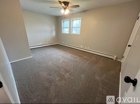 A room with a carpeted floor, a ceiling fan, and a window with blinds.