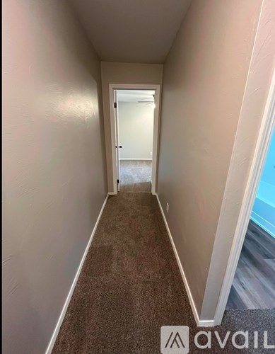 A hallway with carpeted flooring and white walls leading to a door.