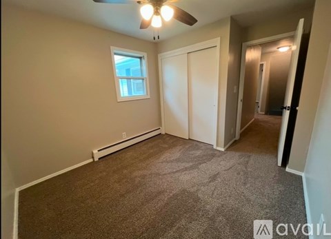 A room with a carpeted floor, a ceiling fan, and a window.