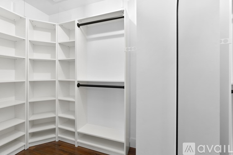 A white walk in closet with shelves and a black rod.
