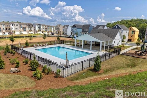 A swimming pool surrounded by a black fence and a grassy area with a few bushes.