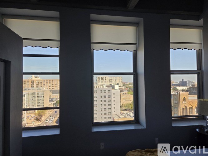 Three windows with white blinds overlooking a cityscape.