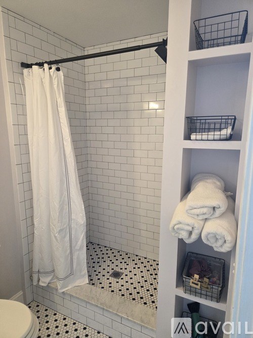 A white towel hangs on a black shower rod in a white tiled bathroom.