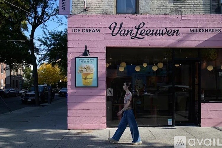 A woman walks past a pink building with a sign that says "Van Leeuwen Ice Cream Milkshakes.".