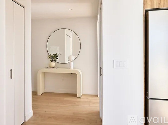 A white framed mirror sits on a white table with a vase of flowers and a white vase on it.