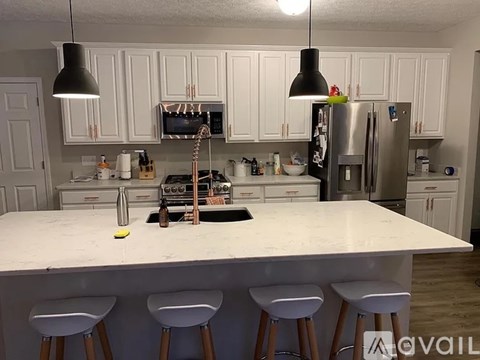 A kitchen with white cabinets and a white island with three stools.
