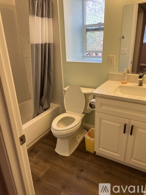 A bathroom with a toilet, sink, and a window with a curtain.
