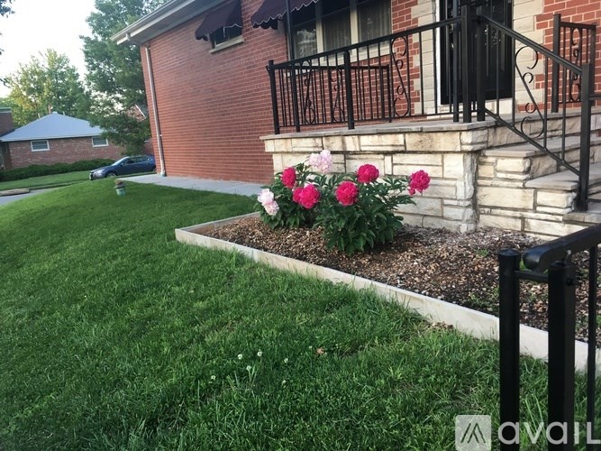 A house with a black railing and a flower bed with pink flowers.