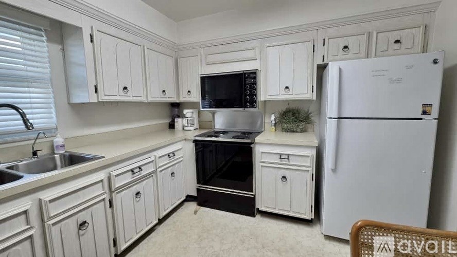 A white fridge sits in a kitchen with white cabinets.