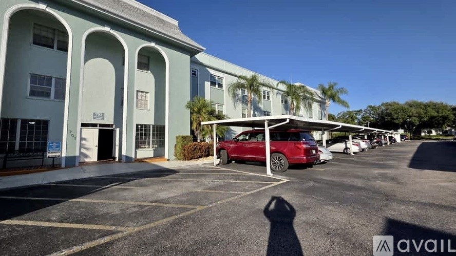 A red car is parked in a parking lot in front of a building with a blue sky in the background.