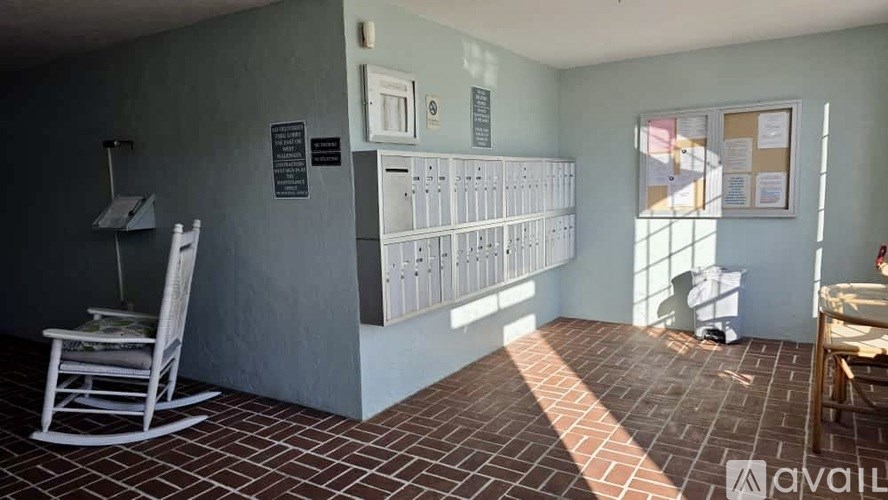 A room with a white rocking chair and a bulletin board on the wall.