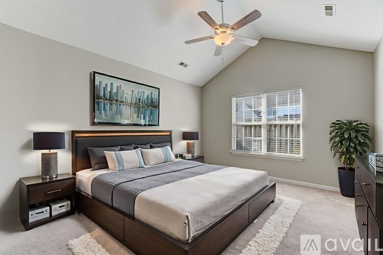 A bedroom with a large bed, a ceiling fan, and a painting on the wall.