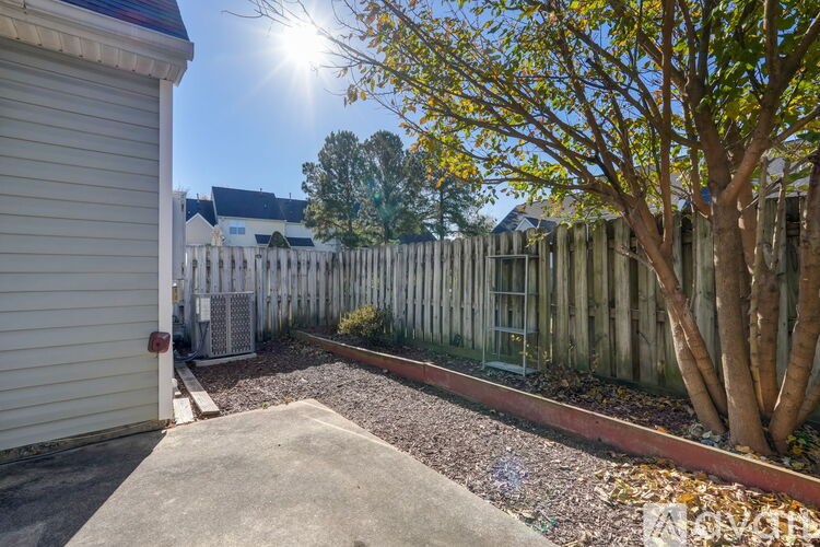 A sunny day in a backyard with a white fence and a tree.