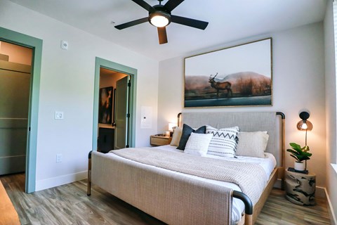 A bedroom with a bed, a ceiling fan, and a painting of a deer on the wall.