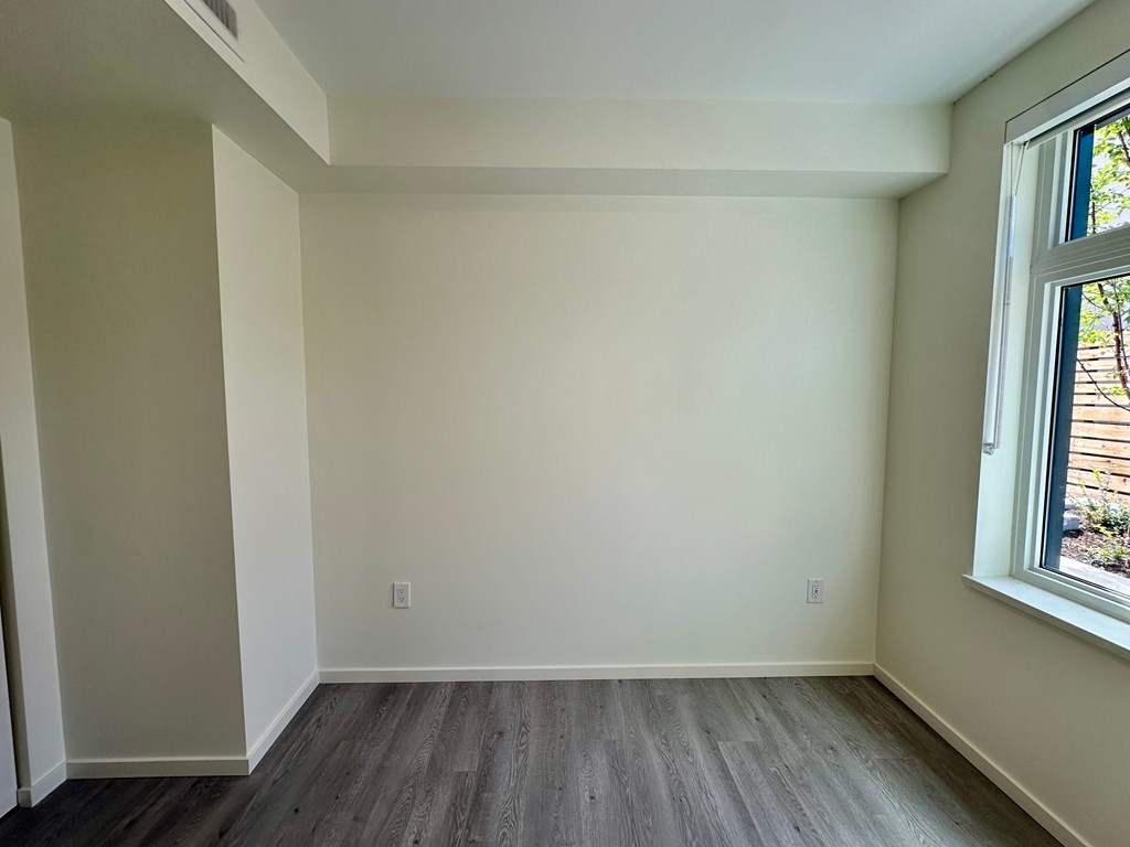 A room with a window on the right side and a wooden floor.