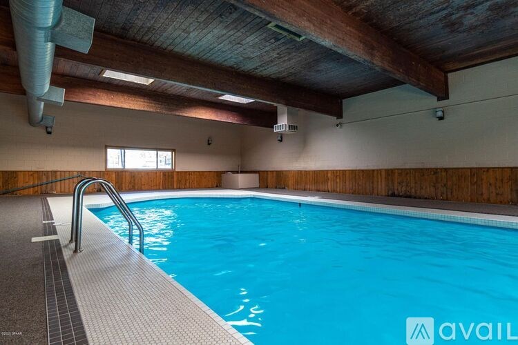 A large indoor swimming pool with a wooden ceiling and a metal ladder on the left side.