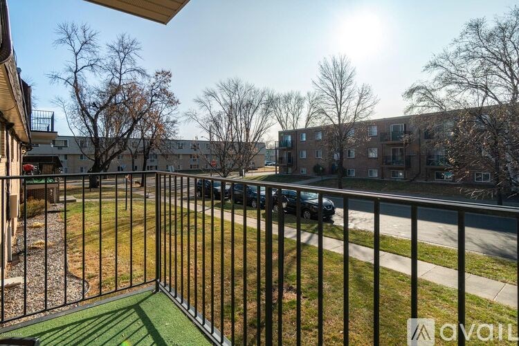 A balcony with a metal railing overlooks a grassy area and apartment buildings.