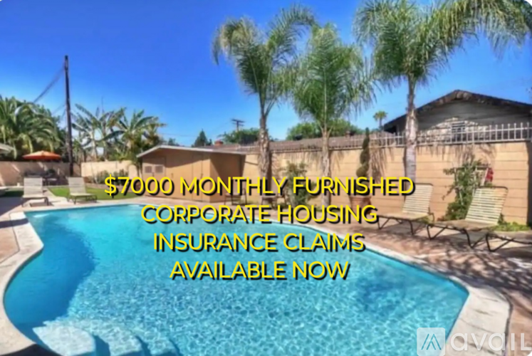A pool surrounded by palm trees and a patio area with chairs and an umbrella.