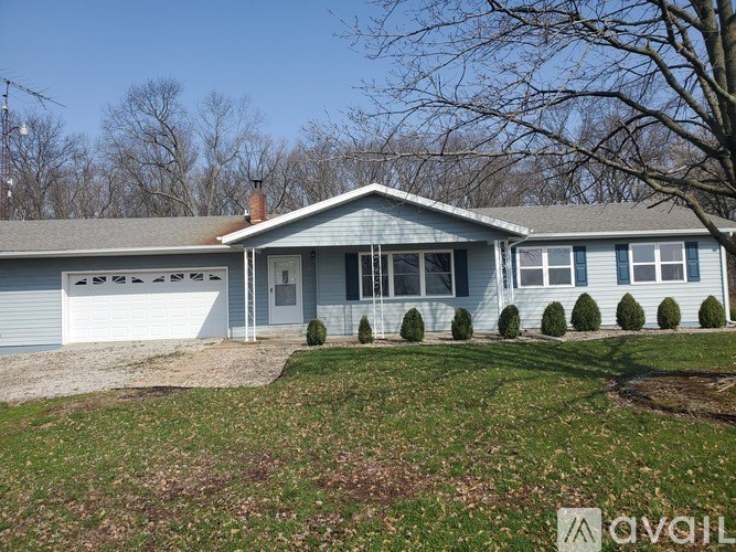 A house with a grey roof and white walls is surrounded by a grassy area and bare trees.