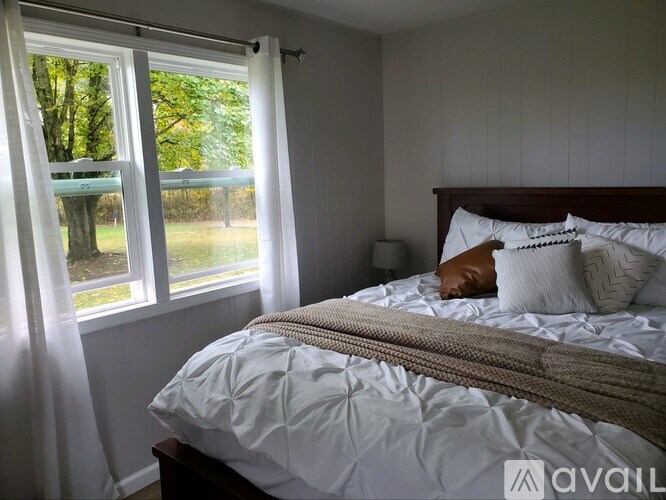 A bedroom with a large bed and a window overlooking a green area.