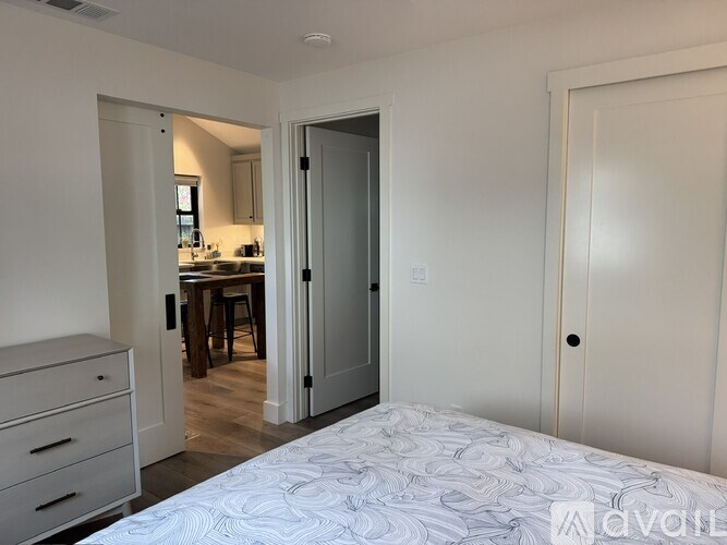 A bedroom with a bed, dresser, and a view into the kitchen.