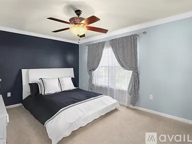 A bedroom with a bed, a ceiling fan, and a window with curtains.