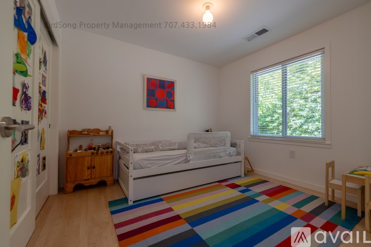 A bedroom with a white bed and a colorful rug.