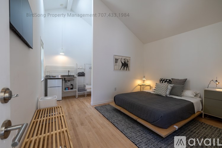 A bedroom with a bed, nightstand, and a small kitchenette.