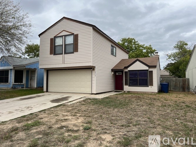 A beige house with a brown roof and a red door is surrounded by a fence and a blue trash can.