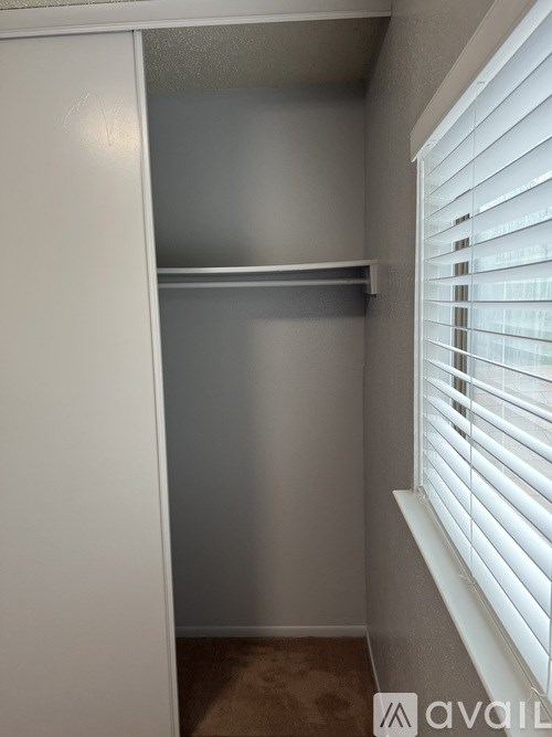 A white closet with a shelf and a window with blinds.