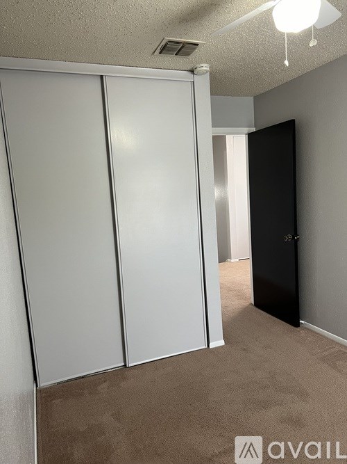 A room with a carpeted floor, a ceiling fan, and a black door.