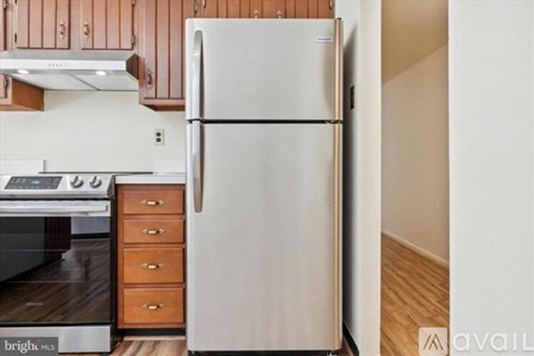 A white refrigerator stands in a kitchen with wooden cabinets and a stove.